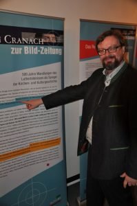 Professor Dr. Albrecht Geck erläutert anhand einer Bildtafel die Aufgabe der von ihm konzipierten Ausstellung, die zur Zeit in der Erlöserkirche in Attendorn zu sehen ist. Foto: Karl-Hermann Ernst